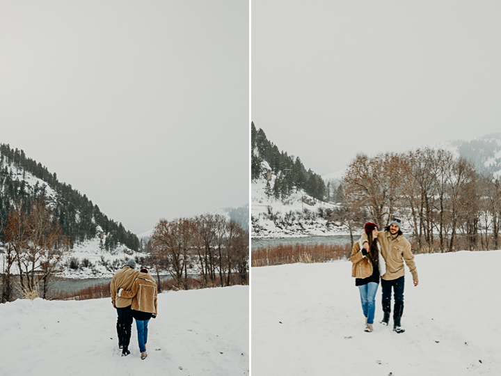 Couple walk together along a frozen Snake River wearing jeans and Vans and smiling